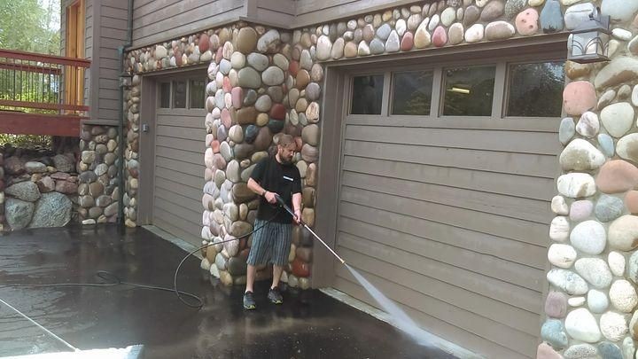 man spraying home and driveway with water to clean